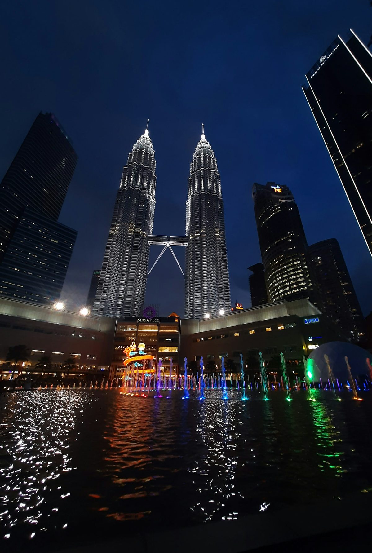 Petronas Towers reflected in a pool at night with dramatic lighting